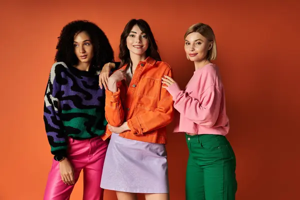 Young beautiful women in stylish clothes pose together, celebrating cultural diversity on an orange background. — Stock Photo