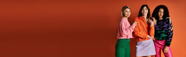 Young beautiful diverse women in stylish clothes posing together on an orange background. — Stock Photo