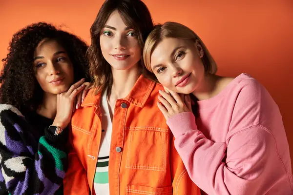 Three young, beautiful multicultural women strike a pose in vibrant clothing against an orange backdrop. — Stock Photo