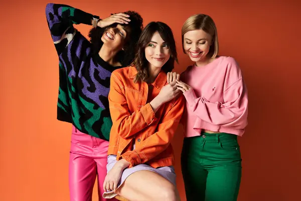 Three young women in vibrant attire striking a pose against an orange backdrop, showcasing friendship and cultural diversity. — Stock Photo