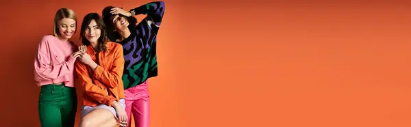 Multicultural women in stylish clothes stand side by side, celebrating friendship and diversity on an orange background. — Stock Photo