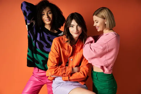Three young women, multicultural and stylish, stand together on an orange background. — Stock Photo