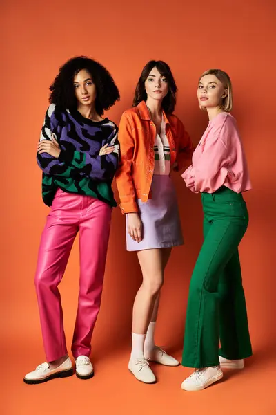 Three young, beautiful women in stylish, multicultural outfits pose on an orange background, celebrating diversity. — Stock Photo