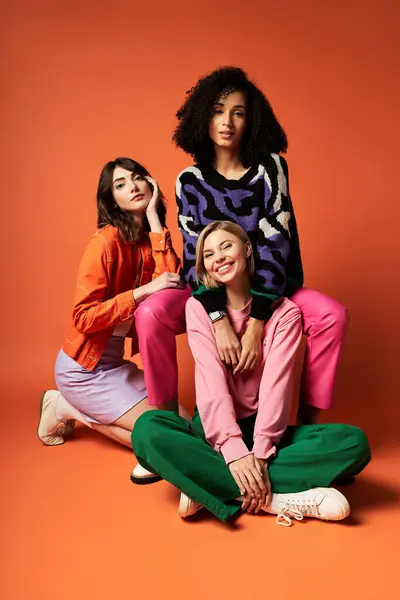 Three multicultural women in stylish attire, showcasing friendship and diversity on an orange background. — Stock Photo