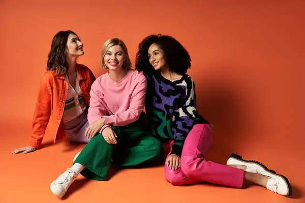 Three young women in vibrant attire showcase friendship and cultural diversity on an orange backdrop. — Stock Photo