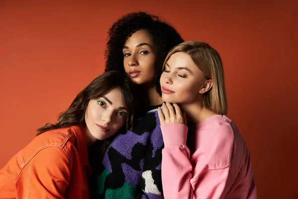 Tre giovani e vivaci donne in abiti alla moda stanno insieme su uno sfondo arancione, mostrando amicizia e diversità culturale.. — Foto stock