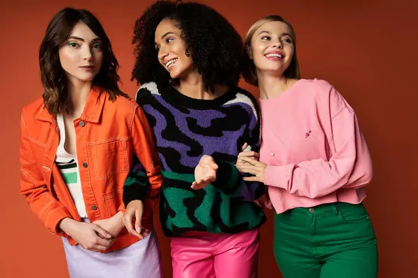 Three young women, each representing a different culture, stand united in stylish outfits against an orange backdrop. — Stock Photo