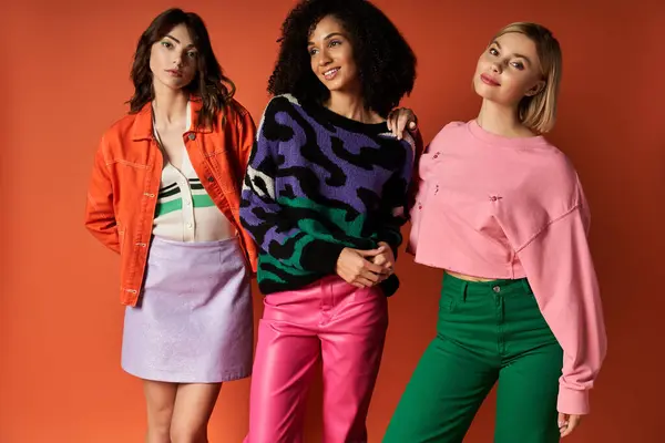 A group of young, beautiful, multicultural women in stylish vibrant clothes pose together on an orange background, showcasing female friendship and cultural diversity. — Stock Photo