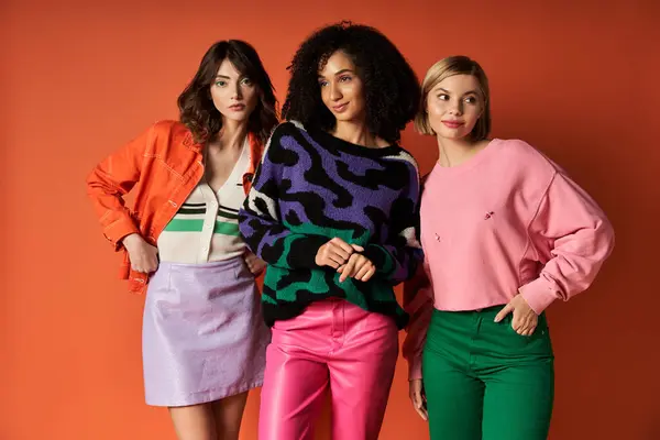 A diverse group of young women in vibrant attire stand together on an orange background, showcasing unity and friendship. — Stock Photo
