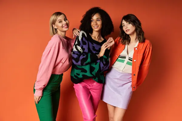 A group of young, beautiful women in stylish, vibrant clothes standing together on an orange background, showcasing friendship and cultural diversity. — Stock Photo