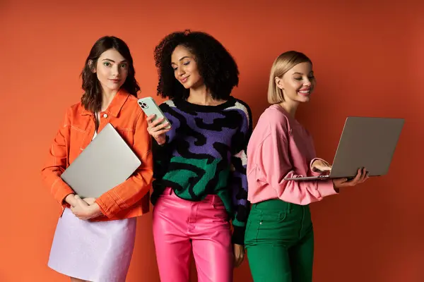 Three young, diverse women stand together holding devices, showcasing modern technology and cultural diversity. — Stock Photo