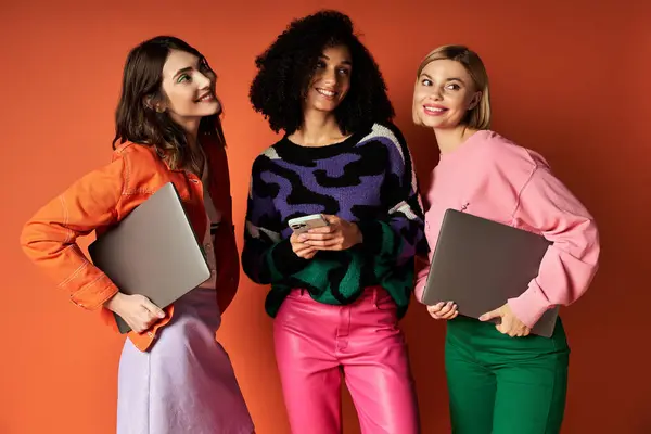 Three young, beautiful, multicultural women stand together, holding laptops, showcasing diversity and empowerment. — Stock Photo