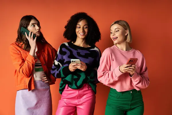 Three young multicultural women in vibrant attire stand united against an orange backdrop, embodying friendship and cultural diversity. — Stock Photo