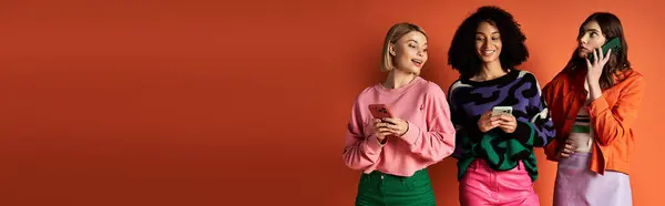 Multicultural women in stylish clothes pose together on orange background. — Stock Photo