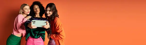 Group of diverse young women in stylish clothes posing for selfie together on orange background. — Stock Photo