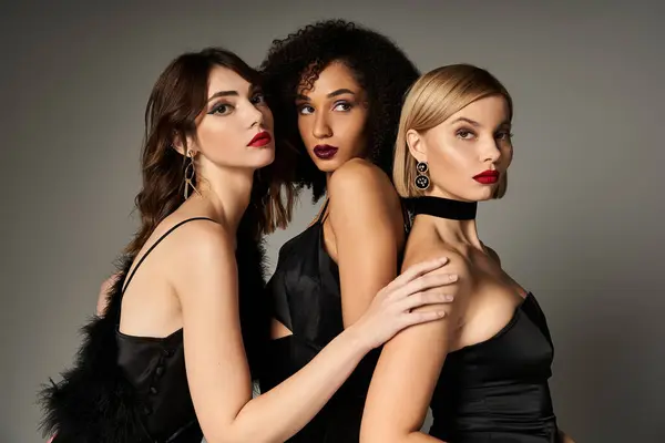A trio of stunning women, each in a chic black dress, striking elegant poses against a neutral backdrop. — Stock Photo