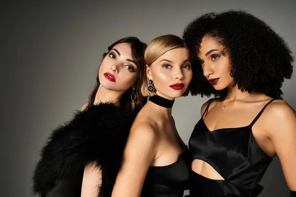 Three stunning women, representing diversity, don elegant black dresses while striking poses against a muted grey backdrop. — Stock Photo
