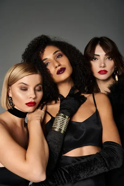 Trois jeunes belles femmes de cultures différentes posent élégamment en tenues noires sur fond gris. — Photo de stock
