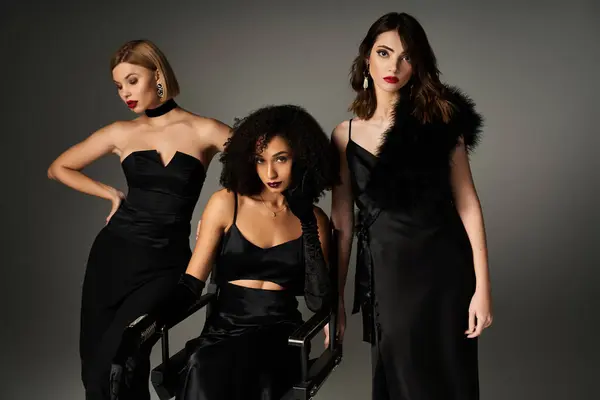 A group of young, beautiful, interracial women in elegant black dresses standing together on a grey background. — Stock Photo