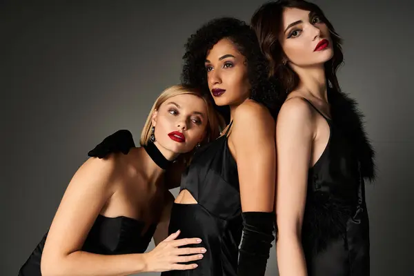 Three young beautiful women, of different ethnicities, elegantly posed for a picture in stylish black dresses. — Stock Photo