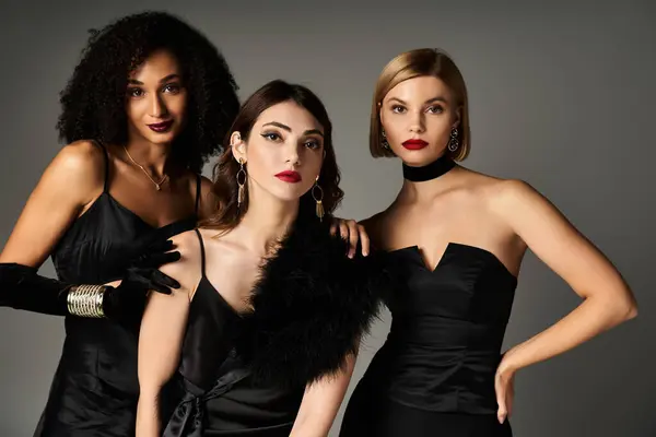 Three women of diverse backgrounds strike a pose in chic black dresses against a neutral backdrop. — Stock Photo