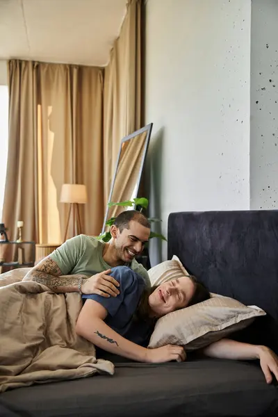 A young gay couple shares a laugh and a cozy moment in bed. — Stock Photo