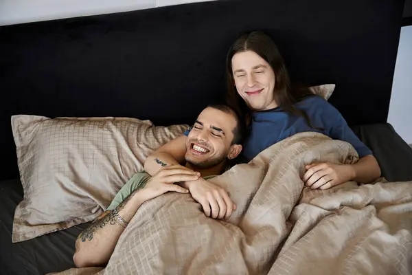 Ein junges schwules Paar kuschelt im Bett, lacht und genießt einen Moment der Intimität. — Stockfoto