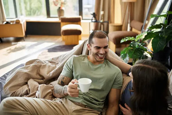 Ein junges schwules Paar verbringt einen gemütlichen Moment zusammen in seinem Schlafzimmer und genießt eine Tasse Kaffee und ein Lachen. — Stockfoto