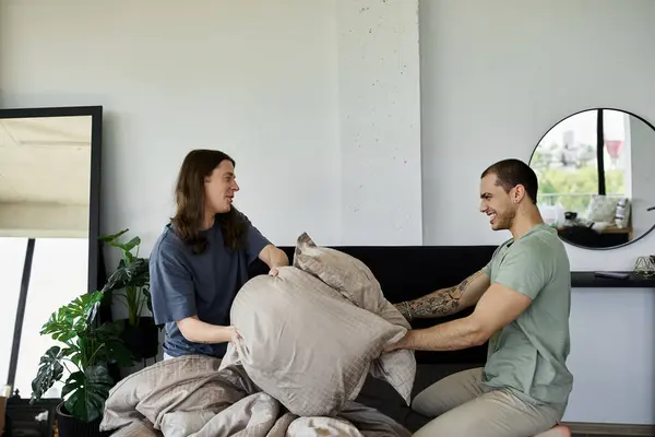 A young gay couple playfully fight with pillows on their bed in their bedroom. — Stock Photo