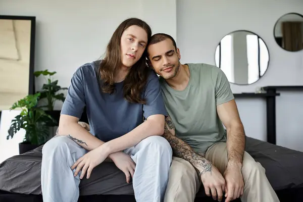 A young gay couple sits together on a bed, enjoying a quiet moment of intimacy in their bedroom. — Stock Photo