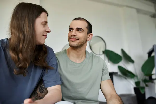 A young gay couple shares a quiet moment of intimacy in their bedroom, their eyes locked in a loving gaze. — Stock Photo
