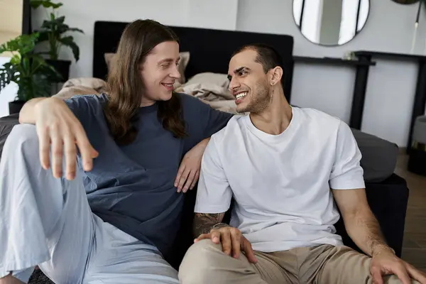 A young gay couple sits on a bed, laughing and sharing a tender moment. — Stock Photo