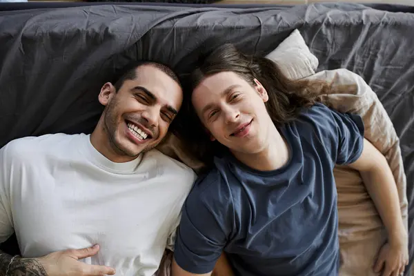 Two young men lie in bed together, laughing and looking at camera — Stock Photo