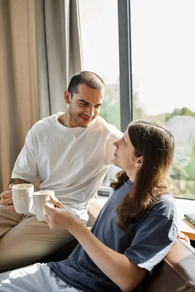 A young gay couple enjoys a cozy morning together in their modern home, sharing coffee and a loving gaze. — Stock Photo
