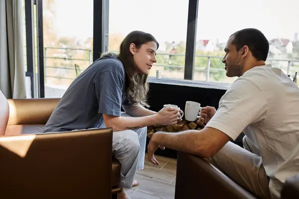 Una giovane coppia gay condivide un momento accogliente insieme in una casa moderna, godendo di una tazza di caffè e conversazione. — Foto stock
