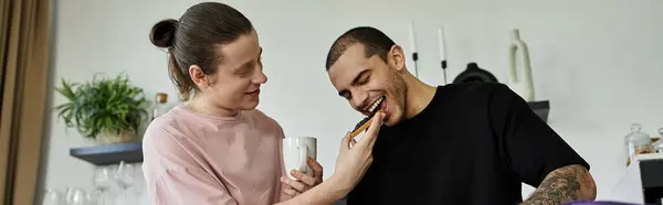 A young gay couple enjoys a cozy moment together in their modern home, sharing a laugh and a bite to eat. — Stock Photo