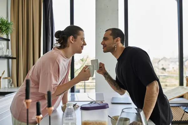 Un jeune couple gay partage un moment tendre autour d'un café dans une maison moderne, les yeux fermés dans un regard aimant. — Photo de stock