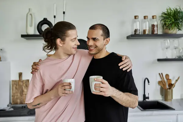 A young gay couple shares a cozy moment in their modern kitchen, enjoying a cup of coffee and embracing each other. — Stock Photo