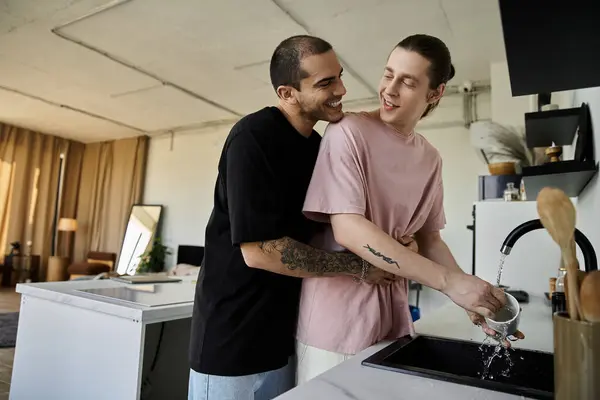 A young gay couple enjoys a moment of playful intimacy while washing dishes in their modern kitchen. — Stock Photo