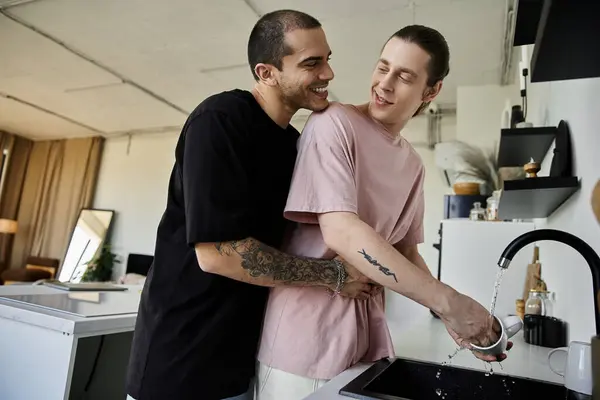 Una giovane coppia gay abbraccia in una cucina moderna, mostrando amore e affetto durante le routine quotidiane. — Foto stock