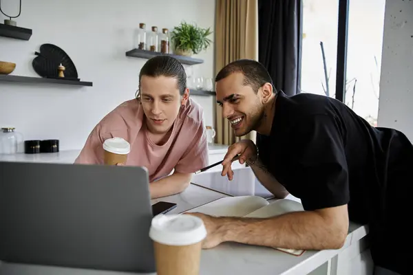 A young gay couple enjoys a coffee break in a modern home, laughing and looking at a laptop together. — Stock Photo