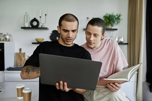 A gay couple relaxes in the kitchen, one browsing on a laptop while the other leans in, creating a warm and intimate scene. — Stock Photo