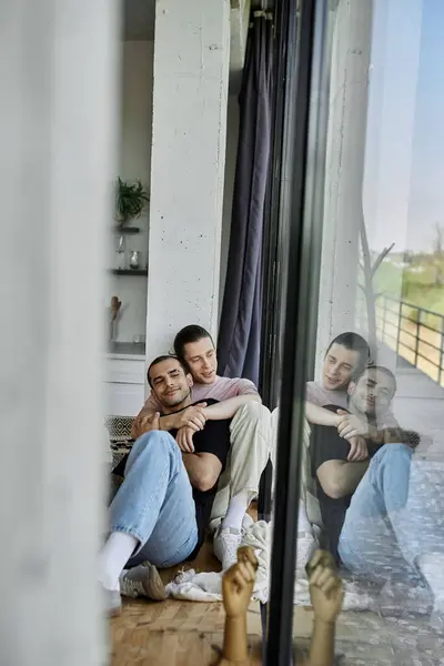Ein junges schwules Paar umarmt sich neben einem großen Fenster in einem modernen Haus. — Stockfoto