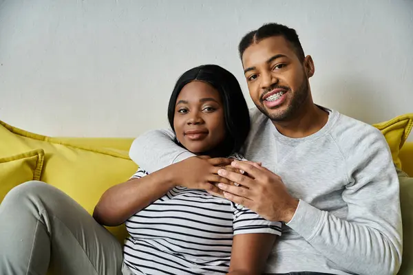 Ein glückliches afroamerikanisches Paar umarmt sich auf einer gelben Couch und genießt die Gesellschaft des anderen. — Stockfoto