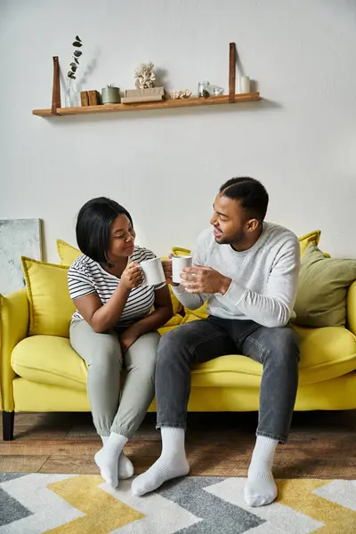 An African American couple enjoys morning coffee on a yellow couch. — Stock Photo