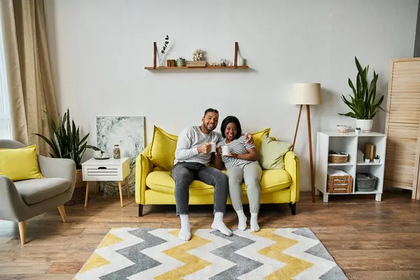 Fröhliches afroamerikanisches Paar genießt Kaffee zusammen auf gelbem Sofa. — Stock Photo