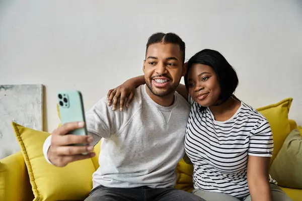 Un couple afro-américain prend un selfie sur un canapé jaune. — Photo de stock