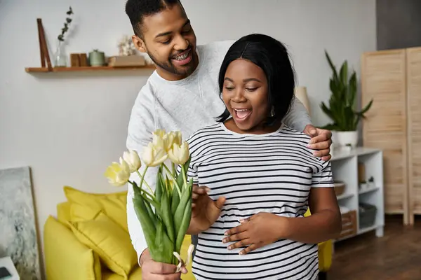 A man surprises his pregnant wife with flowers at home. — Stock Photo