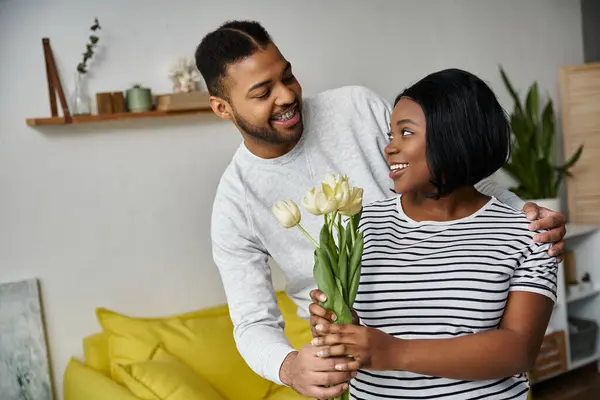 A man presents his wife with white tulips at home. — Stock Photo