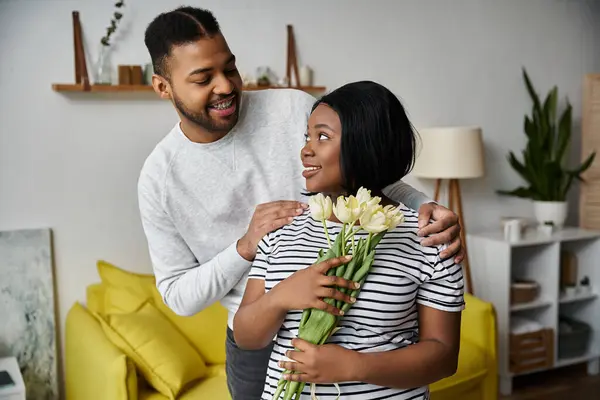 A man presents a bouquet of flowers to his girlfriend at home. — Stock Photo